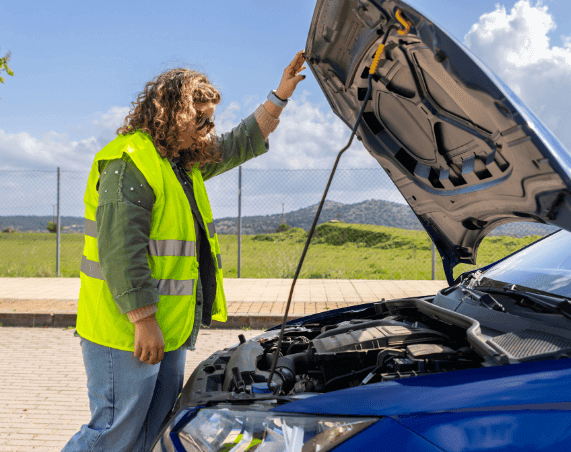 A recovery operator in a hi-vis jacket connecting jump leads under the bonnet of a broken-down car